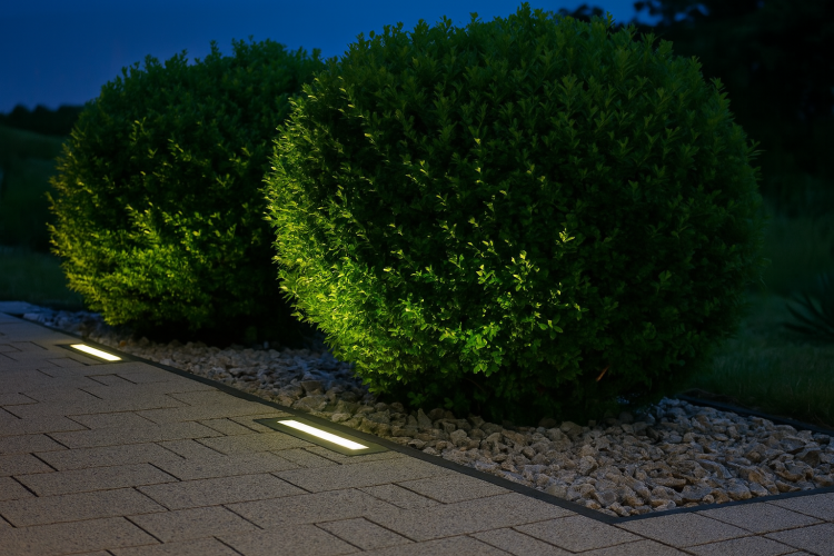 Dwie lampy najazdowe LANDO zamontowane w bruku, efektownie podświetlające krzewy w nowoczesnym ogrodzie..png